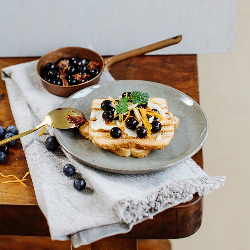 Toasts with hot blueberries, orange zest and almond flakes